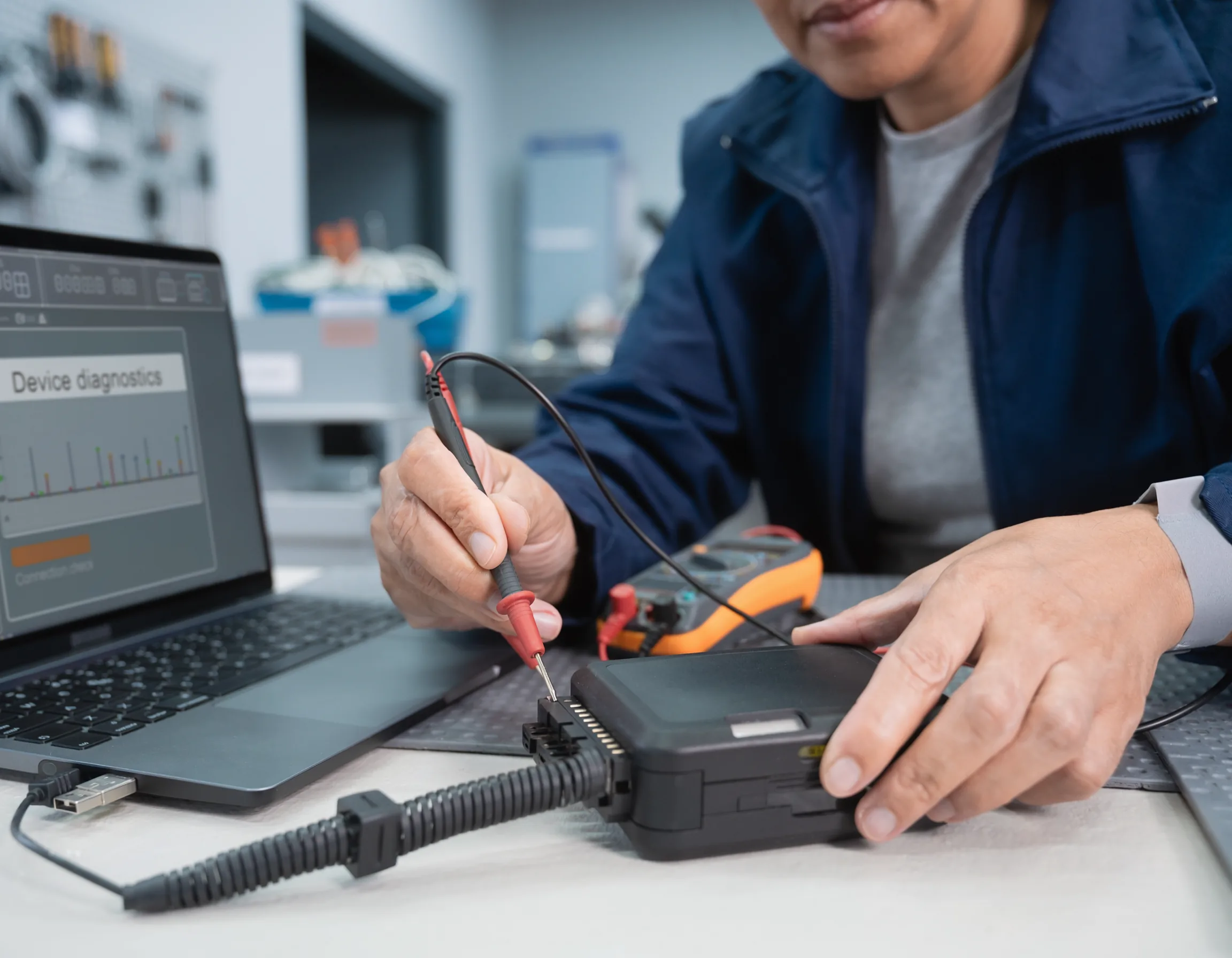 Technician testing a fleet tracker and its connection leads beside a laptop displaying device diagnostic results