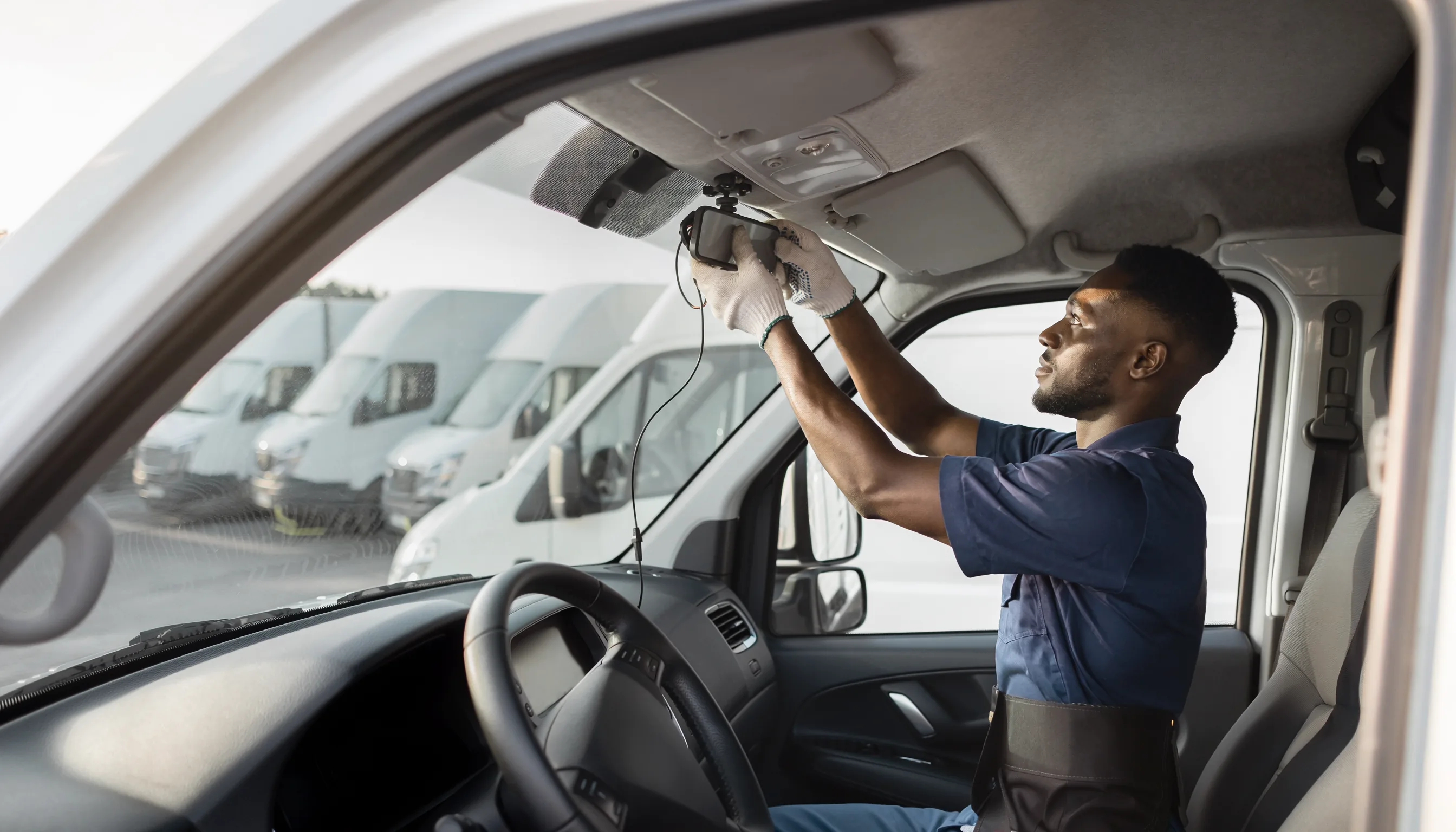 Fleet technician installing a compact dash camera inside a delivery van as a connected vehicle fleet is prepared for deployment